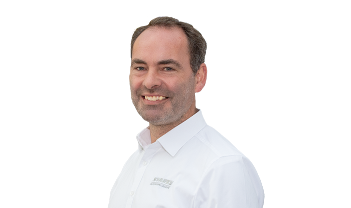 Portrait eines Mitarbeiters mit kurzen Haaren und weißem Hemd. 